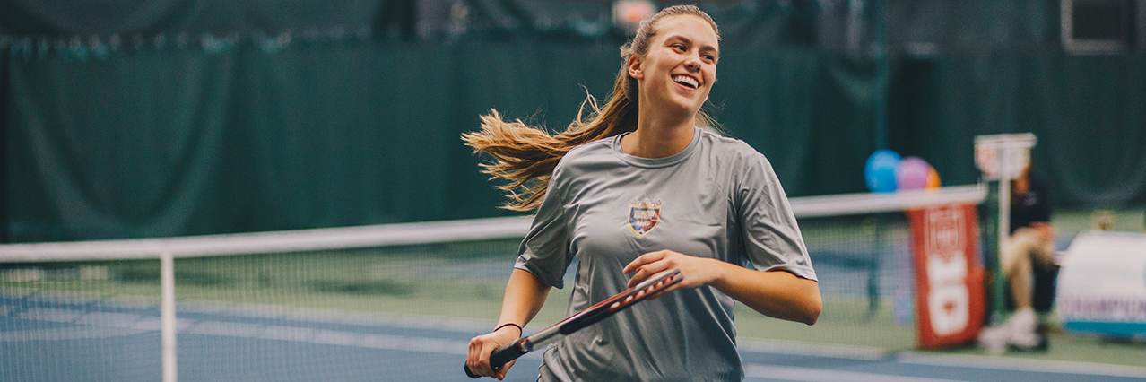 A girl smiles while running on a tennis court.